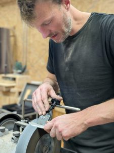 Artisan coutelier en train d’affûter un couteau à l’eau avec réglage précis de l’angle à la Coutellerie Bermudes près de Chambéry en Savoie.
