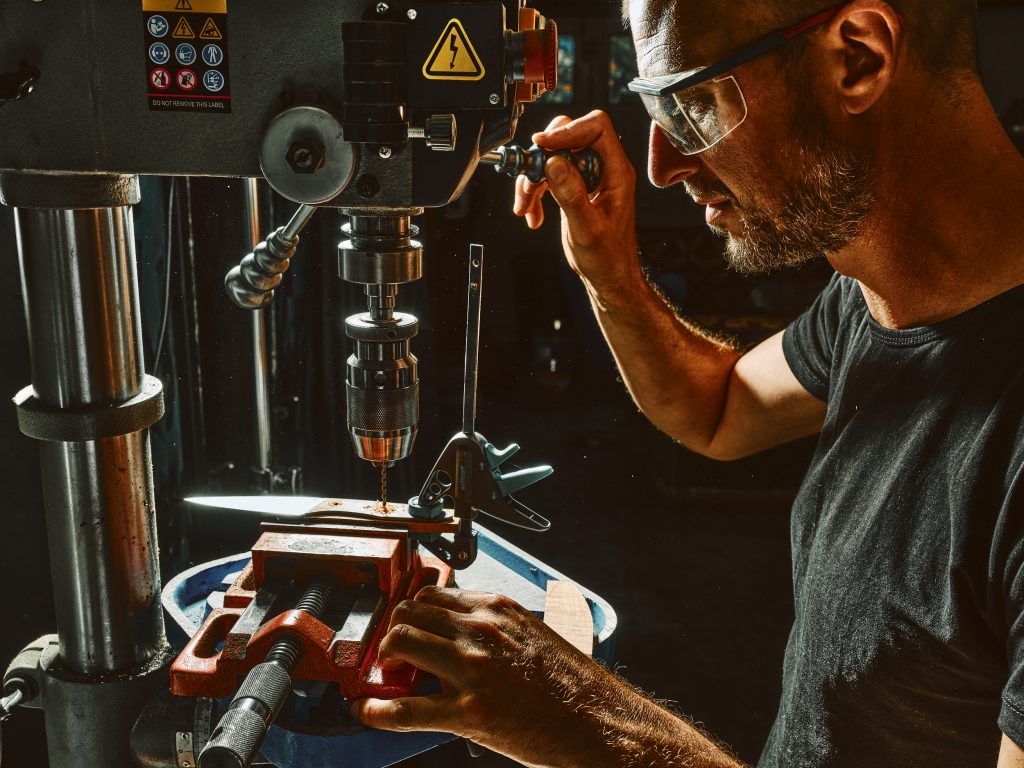 Coutelier artisanal en Savoie perçant des plaquettes de bois pour fabriquer un manche de couteau de cuisine
