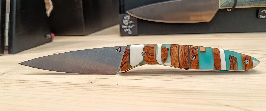 Couteau de table artisanal modèle n°5 avec manche en bois d’olivier, résine teintée translucide bleue et Corian®, fabriqué à la Coutellerie Bermudes en Savoie près de Chambéry.