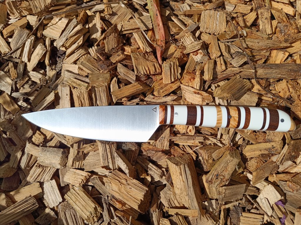 Couteau de cuisine artisanal modèle n°7 demi-chef en Corian®, noyer et loupe de frêne – Coutellerie Bermudes Texte alternatif (ALT) Couteau de cuisine artisanal modèle n°7 demi-chef avec manche en Corian®, noyer stabilisé et loupe de frêne stabilisée, fabriqué à la main à la Coutellerie Bermudes près de Chambéry en Savoie.