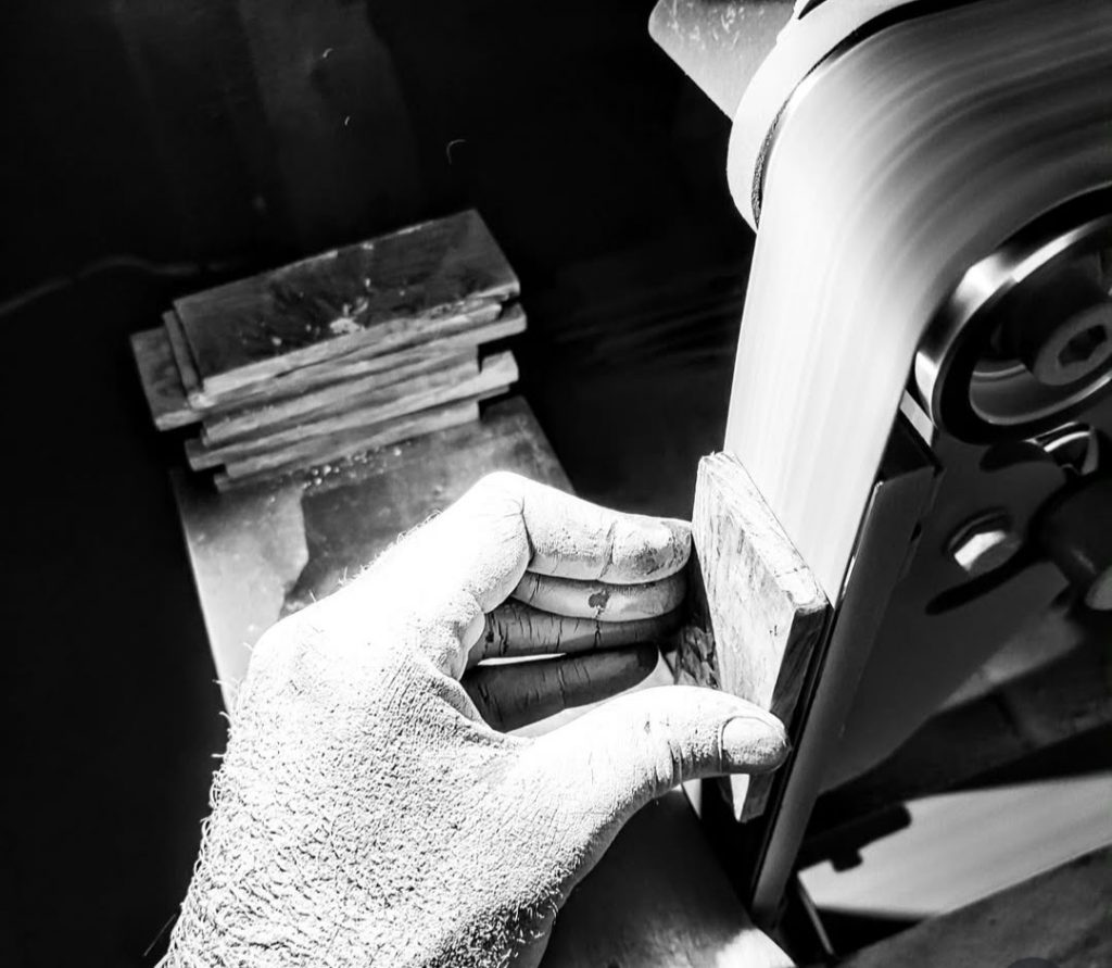 Artisan coutelier en train de poncer une plaquette de manche de couteau pour l’ajuster avant montage dans son atelier près de Chambéry en Savoie.