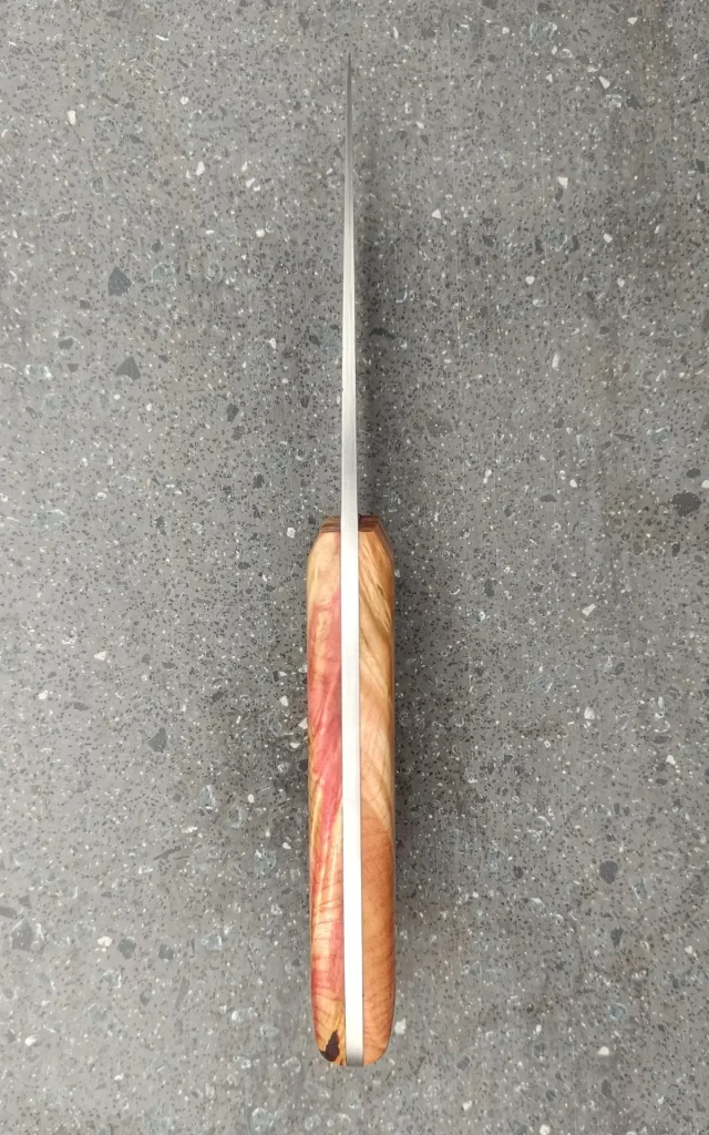 Vue du dos d’un couteau de cuisine artisanal avec manche en bois stabilisé teinté rouge